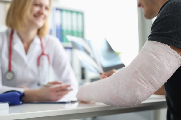 Paciente masculino con vendaje en el brazo sentado en la cita del traumatólogo primer plano escalado